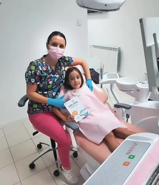 Doktorka i nasmejana devojčica sa diplomom u stomatološkoj stolici